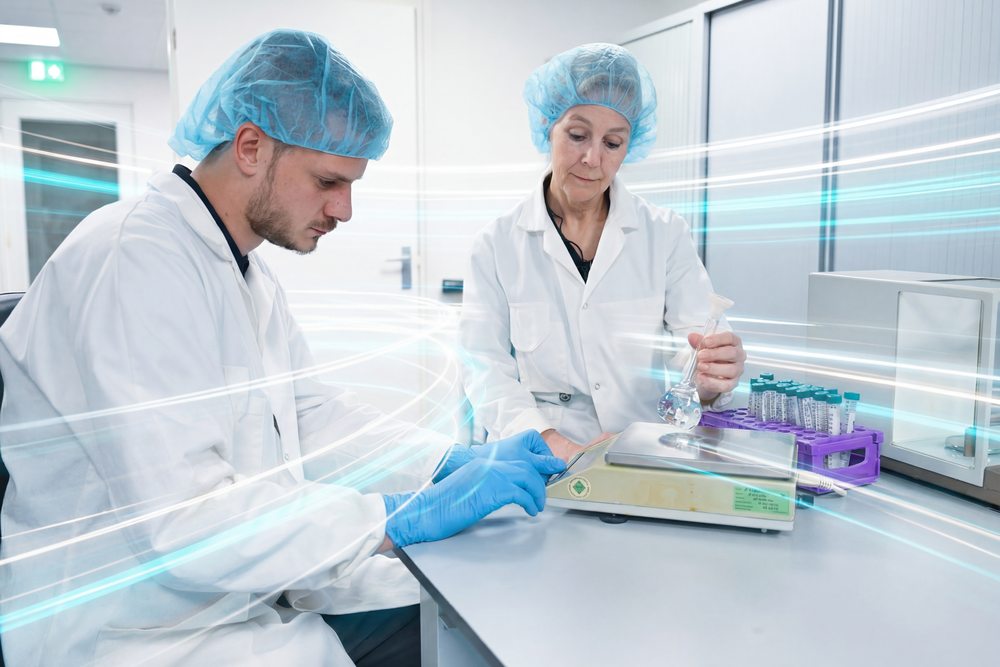 Two lab technicians weigh a sample at the bench, racks of sample vials beside them.